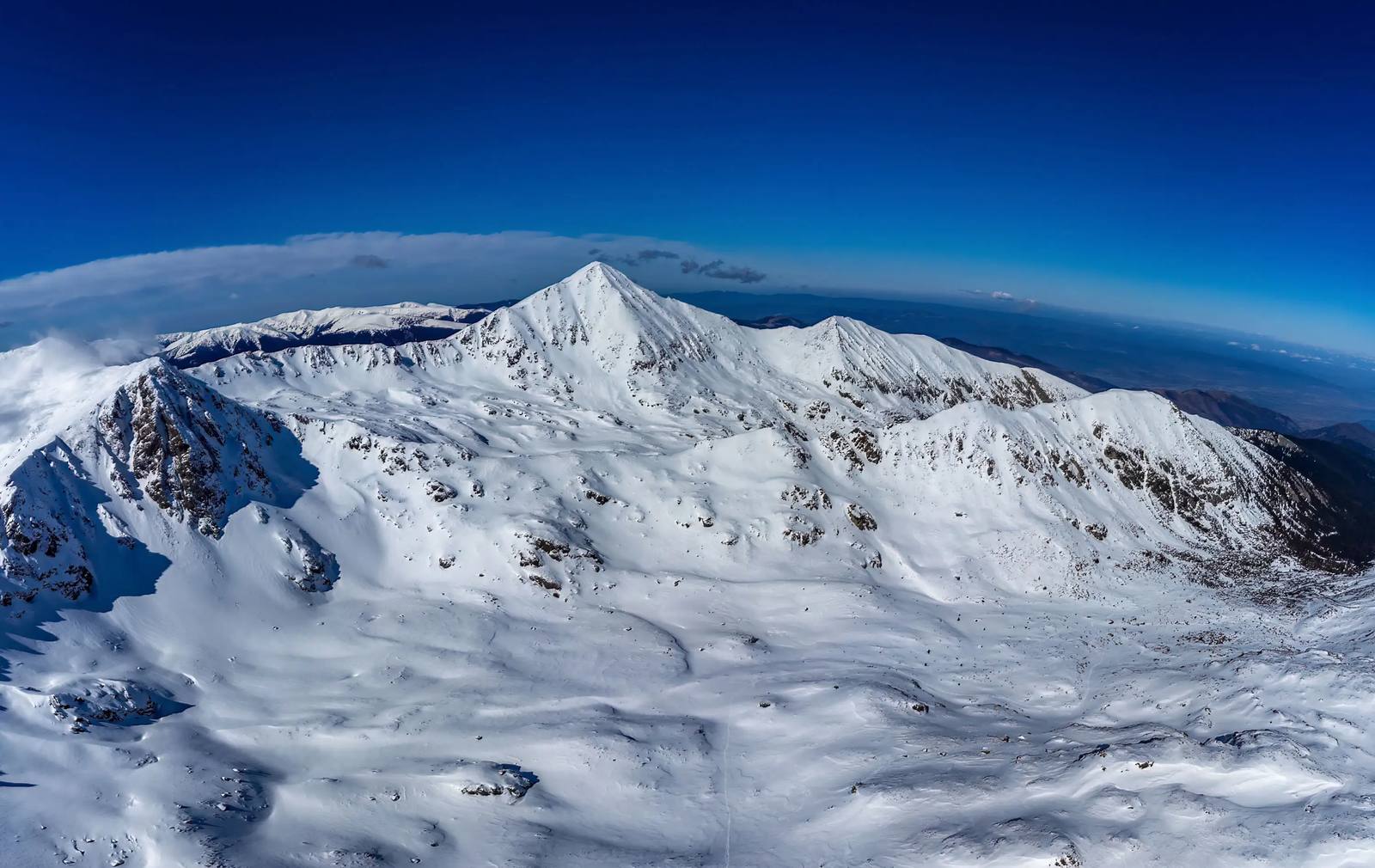 Panoramă de iarnă în Munții Retezat, cu creste acoperite de zăpadă sub un cer albastru